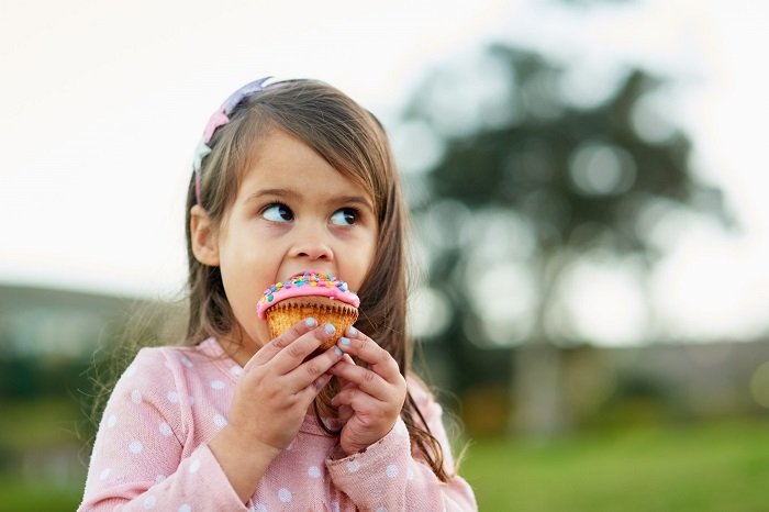Bambina che mangia un muffin. Sapore dolce